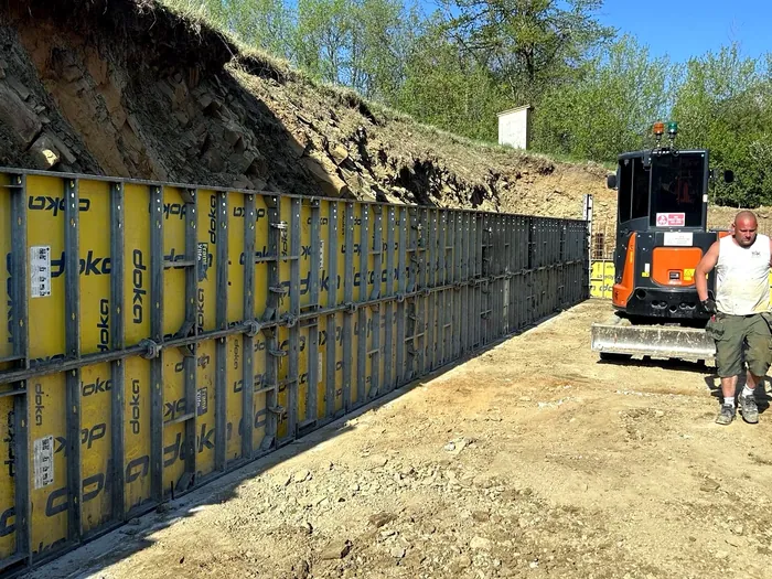 Debnenie oporného múru a stavebná mechanizácia na svahovitom pozemku