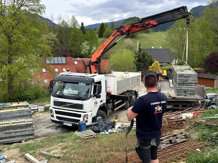 Žeriav na nákladnom aute vykladá debnenie na stavbe oporného múru