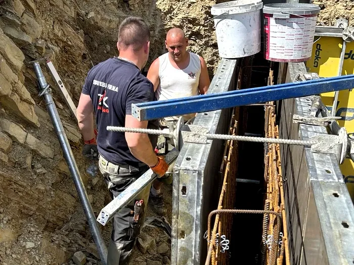 Pracovníci montujú debnenie a výstuž oporného múru v úzkom výkope